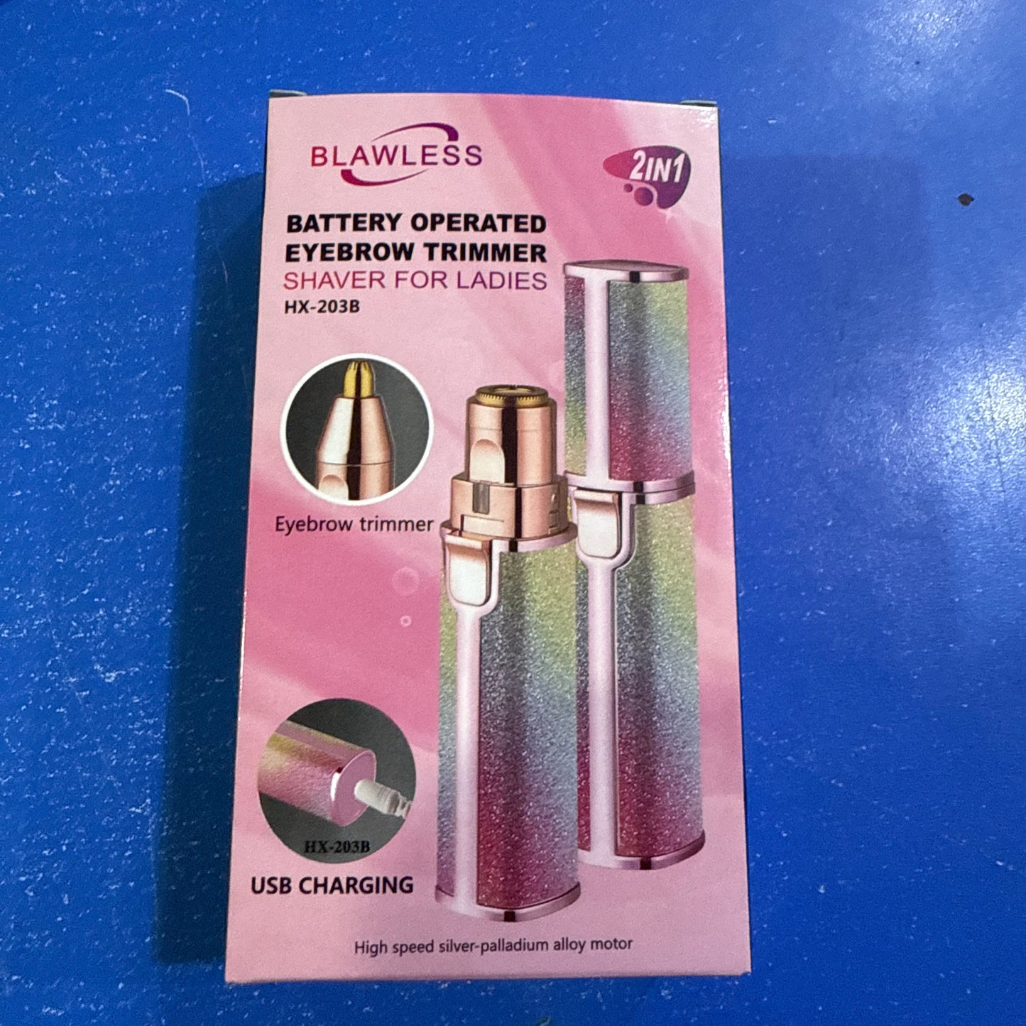 A pink retail box for a BLAWLESS 2-in-1 battery operated eyebrow trimmer and shaver for ladies, shown on a blue surface. The packaging features product images and text including 'Battery Operated Eyebrow Trimmer', 'Shaver for Ladies', and 'USB Charging'.