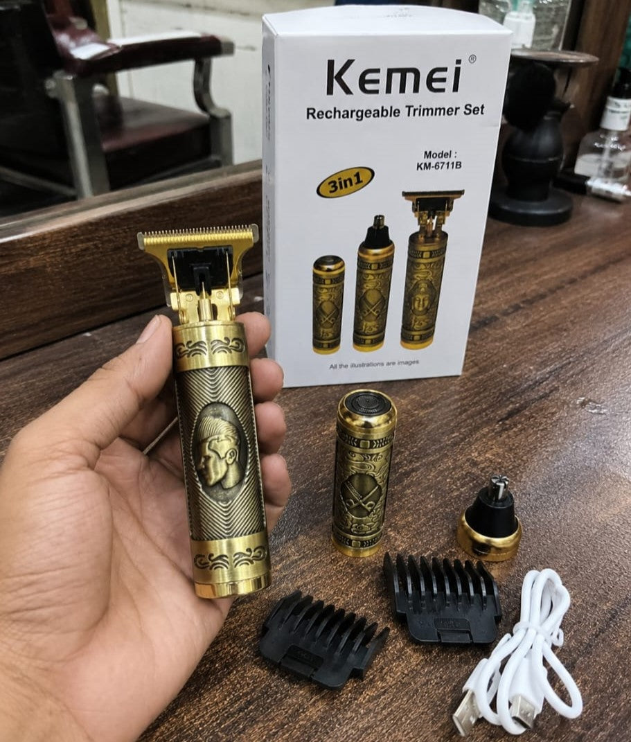A hand holds a gold-colored Kemei rechargeable trimmer with a decorative handle, with its accessories (guide combs, charging cable, battery) and the product box displayed on a wooden table.