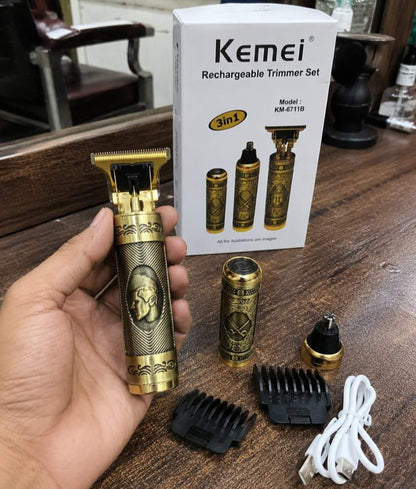 A hand holds a gold-colored Kemei rechargeable trimmer with a decorative handle, with its accessories (guide combs, charging cable, battery) and the product box displayed on a wooden table.